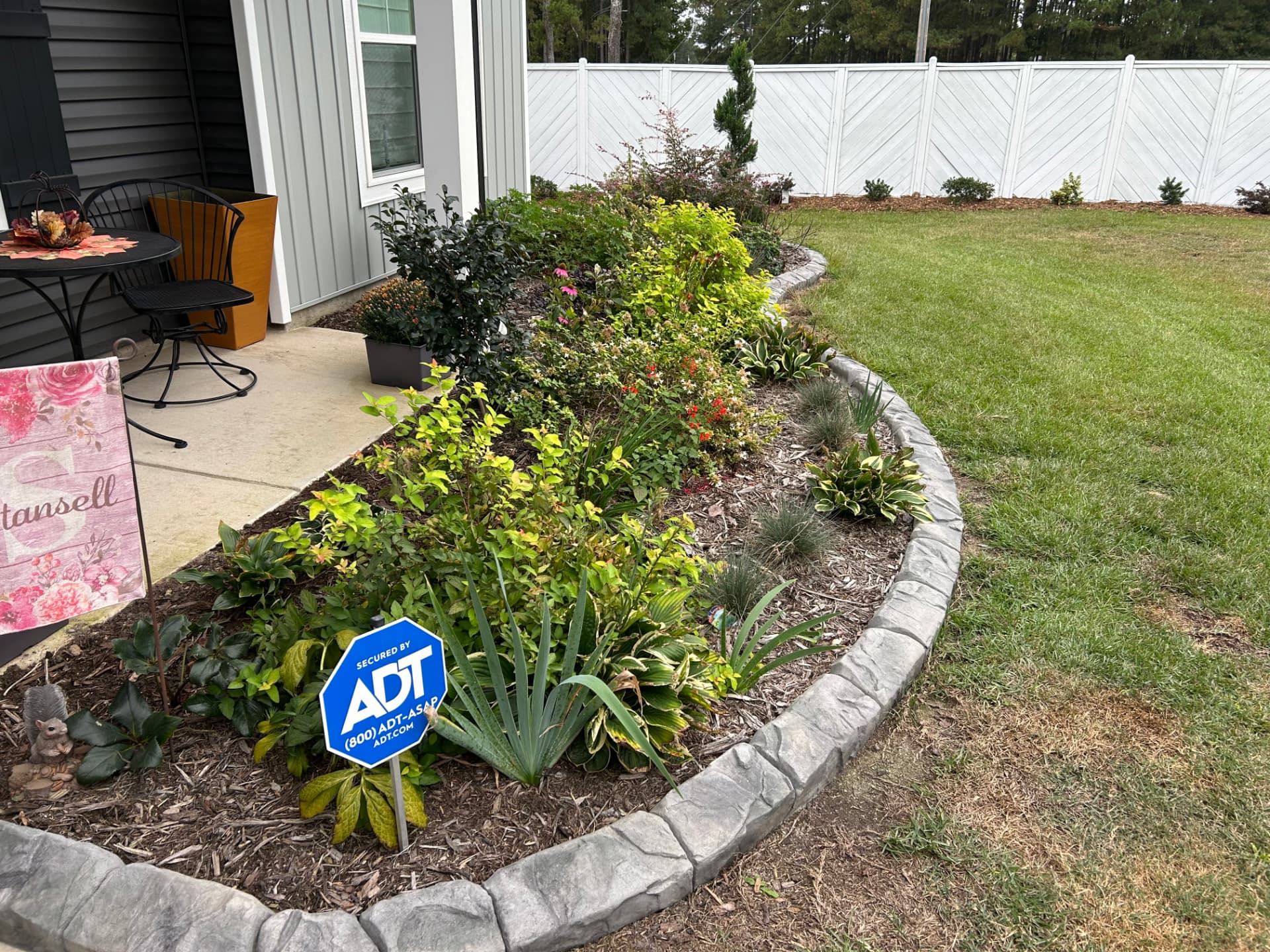 Curved garden bed with flowering shrubs, fresh mulch and stone edging beside a lawn